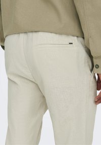 Lichtbeige linnen broek met een subtiele textuur, voorzien van een achterzak en een relaxte pasvorm. Gecombineerd met een olijfgroen shirt.