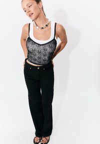 Svarta vida byxor i kombination med en svart spetscroppad topp över en vit linne. Accessoarer inkluderar ett kraftigt silverhalsband. Släta texturer.