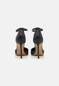 Sandales à talons hauts noires avec une bride de cheville, finition en cuir lisse, dos ouvert, et accents beiges sur la semelle avec un logo.