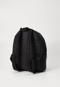 Black padded backpack with dual adjustable straps, a smooth texture, rounded shape, and a tag featuring the letters "DKN" on one strap.