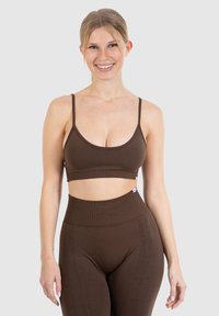 Brun, ribbet sports-bh med tynde stropper og en bred kant, parret med high-waisted brune leggings, der har en subtil tekstur.