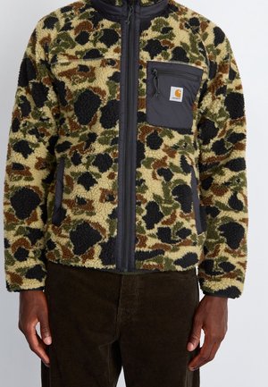 Man wearing a zip-up fleece jacket with black, green, and brown camouflage pattern and a zippered chest pocket with logo patch.