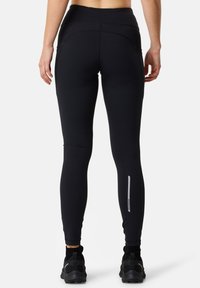 Black athletic leggings feature a high waistband, smooth texture, and reflective detailing on the lower leg for visibility.