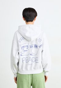 Hallidegriiga kapuutsiga ja laia varrukaga hall dressipluus, mille seljaosas on sinine kassi illustratsioon ja tekst "VABADUS ON RAHU".