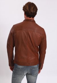 Giacca di pelle marrone con un design aderente, caratterizzata da un colletto alto e polsini con zip. Tessuto liscio con dettagli di cucitura sottili.