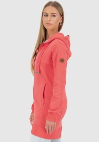 Korallfarbener Hoodie mit Reißverschluss, Seitentaschen und Kapuze mit Kordelzug. Verfügt über eine strukturierte Oberfläche und ein kleines rundes Logo am Ärmel.