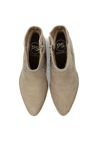 Beige suède enkellaarsjes met spits toelopende neuzen. Voorzien van gestikte details en ritsen aan de zijkanten. Soepele textuur met een tankleurige zool.