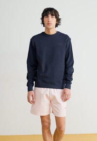 Marineblå sweatshirt med rund hals og ribbede manchetter, parret med lyserøde shorts med et lille logo. Glat tekstur, afslappet pasform.