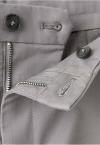 Gros plan de la ceinture d'un pantalon gris montrant des boutons noirs, des boutonnières et une fermeture éclair métallique partiellement ouverte.