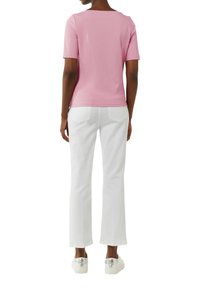 Rosa Kurzarmoberteil und weiße gerade Hose. Das Oberteil hat einen weiten Halsausschnitt; die Hose besitzt zwei Gesäßtaschen und einen sauberen Abschluss.