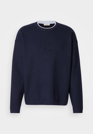 Námořnický modrý pletený svetr s kulatým výstřihem, ribbovaným límcem a jemně vyšívaným logem "ck" na přední straně. Dlouhé rukávy, volný střih.