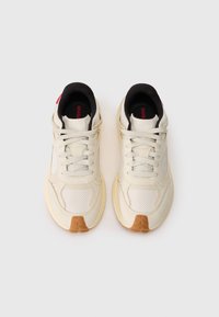 Zapatillas beige claras con texturas de malla y suaves, forro interior negro, cordones planos y suela de goma. Con detalles de marca en rojo.