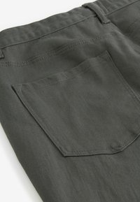 Gros plan sur un tissu en denim gris foncé montrant une poche arrière avec des coutures apparentes et une passants de ceinture à la taille.