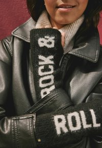 Czarne dzianinowe rękawice z białym napisem "ROCK & ROLL", zestawione z czarną skórzaną kurtką i beżowym swetrem.