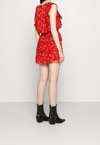 Rotes Blumenkleid mit geschichteten Rüschensäumen, tailliertem Bund und ausgestellt Rock, kombiniert mit schwarzen Knöchelstiefeln.