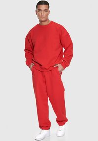 Rød sweatshirt og matchende joggers i blødt materiale, med afslappet pasform og ribbede manchetter, parret med hvide sneakers.