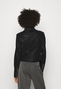 Giacca cropped in pelle nera con schiena texturizzata, maniche con cerniera e un'etichetta vicino al colletto. Design semplice con vestibilità sartoriale.