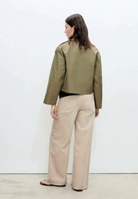 Olive green cropped jacket with long sleeves, paired with wide beige pants. Smooth fabric, minimal hardware, and a simple design.