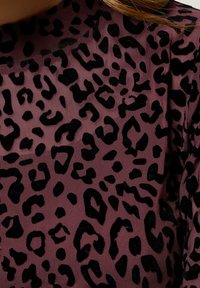 Przezroczysty materiał w kolorze mauve z czarnym wzorem w panterę. Wzór składa się z różnych kształtów i tekstur, prezentując wypukłe akcenty z weluru.