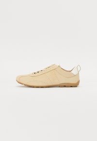 Beige semsket sko med rund tå, perforerte detaljer og en kontrastfylt hvit hæltab. Snøring design med gummisåle.