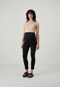 Μπεζ ριγέ φανελάκι συνδυασμένο με μαύρα ελαστικά κολάν, με ψηλή μέση για στήριξη. Το μοντέλο φορά μαύρα σανδάλια χωρίς φτέρνα.