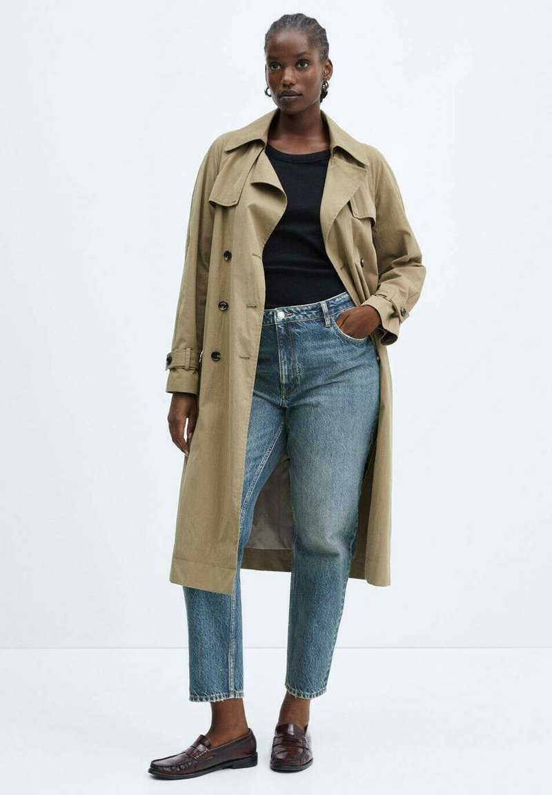 Beiger Trenchcoat, schwarzes Top, hoch sitzende Jeans, braune Slipper. Der Trenchcoat hat große Revers und Knöpfe, mit einem entspannten Schnitt und mittellanger Länge.