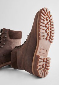 Bottes en cuir marron avec un col en daim à la cheville, un bout rond et une semelle en caoutchouc texturée dotée de motifs de rainures profondes pour une meilleure adhérence.
