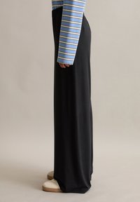 Pantalons larges noirs avec une taille élastique, associés à une chemise à manches longues rayée bleu et blanc et des baskets crème. Texture lisse.