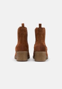 Brown suede ankle boots with a textured heel and pull tabs at the back, featuring a smooth finish and rounded toe design.