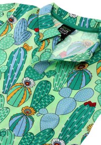 Groene poloshirt met een cactuspatroon in verschillende tinten, met blauwe accenten en bloemdetails. Gemaakt van biologisch katoen.