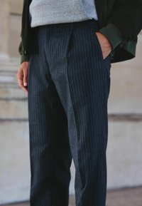 Tumši svītrainie bikses, izgatavotas no teksturēta auduma. Iespējas leņķiskas kabatas, klasiskā piegriezuma un daļēji redzams pelēks kapuci.