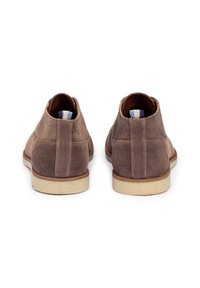 Stivali alla caviglia in suede marrone con una superficie liscia, suola in gomma beige e un tab di estrazione a righe blu e bianche sul retro.