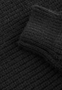 Maglia nera a trama tessuta con polsino a coste; presenta un motivo intrecciato con una leggera peluria, indicando calore e uno spessore medio.