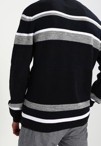 Maglione a righe nere e grigie con dettagli bianchi. Realizzato in materiale lavorato a maglia, presenta una vestibilità comoda e polsini a coste. Vista posteriore mostrata.