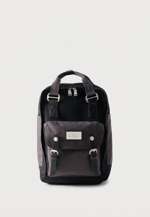 Sac à dos noir et gris avec doubles poignées supérieures, poche à rabat avant avec boucles, et double fermeture éclair sur fond uni.