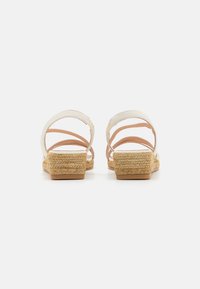 Sandales blanches en cuir avec plusieurs fines bandes, talons en jute tressé et une petite base en bloc. Texture lisse avec une couleur beige naturel.