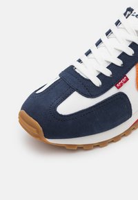 Blaue Wildlederschuhe und weiße Stoff-Sneaker mit Gummisohle. Mit weißen Schnürsenkeln und einem roten Logo-Tag. Runde Zehenpartie und gepolstertes Zunge.