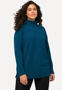 Mėlynas megztas turtleneck megztinis su ilgomis rankovėmis, šoninėmis plyšimis ir tekstūruotu apvadu. Minkšta medžiaga su laisvu siluetu.