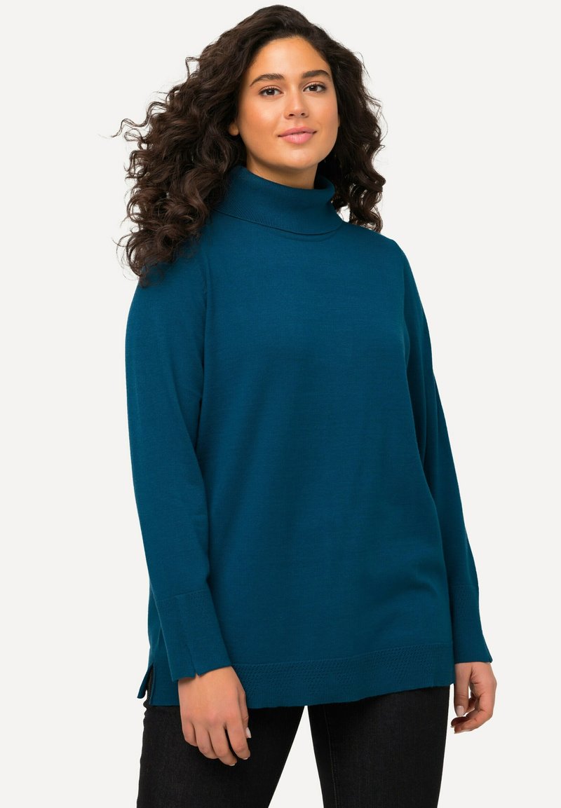 Mėlynas megztas turtleneck megztinis su ilgomis rankovėmis, šoninėmis plyšimis ir tekstūruotu apvadu. Minkšta medžiaga su laisvu siluetu.