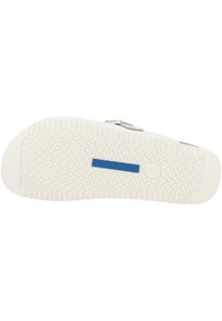 Suola di sandali in gomma bianca con un motivo testurizzato, caratterizzata da un'etichetta blu "Birkenstock" e una fibbia argentata sulla parte superiore della scarpa.