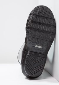 Semelle de botte en caoutchouc noir avec un profil texturé. Présente le logo de la marque et des détails de taille. Fini lisse avec des accents surélevés le long des bords.