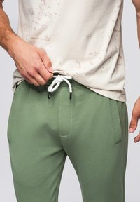 Groene katoenen joggers met een elastische tailleband en witte trekkoord, gecombineerd met een crèmekleurig T-shirt met lichte spetterpatronen.