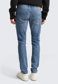 Vaqueros de denim azul claro con corte ajustado, diseño de cinco bolsillos y costuras en contraste. Presenta una etiqueta de cuero con marca en la cinturilla.