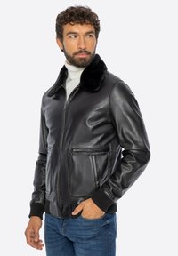 Zwarte leren bomberjack met een bontkraag, twee zakken aan de voorkant, geribde manchetten en een gladde afwerking. Draagt over een lichte coltrui.