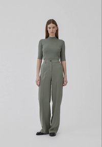 Top fitted verde chiaro con maniche corte abbinato a pantaloni larghi a vita alta dello stesso tessuto e colore; scarpe nere flat.