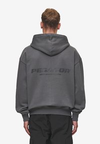 Mörkgrå oversize hoodie med en framsida grafiken "PEGADOR" i matt finish och snodd i huvan; mjuk textur, avslappnad design.