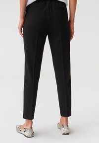 Svarta byxor med elastisk midja och två bakfickor, med en skräddarsydd passform och tapered bendesign. Bärs med snäcktryckade slip-on-skor.