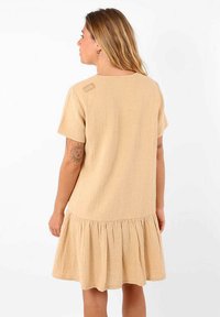 Robe beige à manches courtes en matériau texturé, avec un ourlet évasé et un petit détail d'accent près du col.