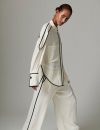 Λευκό πουκάμισο και παντελόνι με μαύρο τελείωμα. Το πουκάμισο έχει τσέπη, φαρδιές μανσέτες και μεταξένια υφή. Χαλαρή γραμμή με καθαρό σχέδιο.