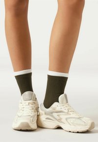 Hvide mesh- og syntetiske sneakers med teksturerede detaljer, parret med olivengrønne ribbede sokker med en hvid manchet.